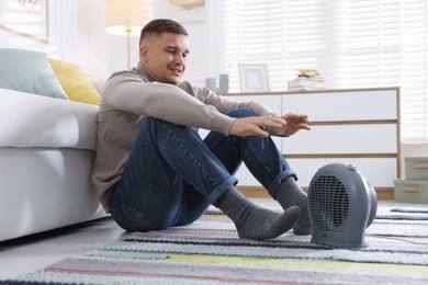 Photo of Young man near electric heater on floor at home