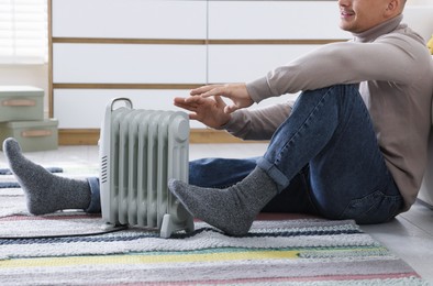 Photo of Young man near electric heater on floor at home, closeup