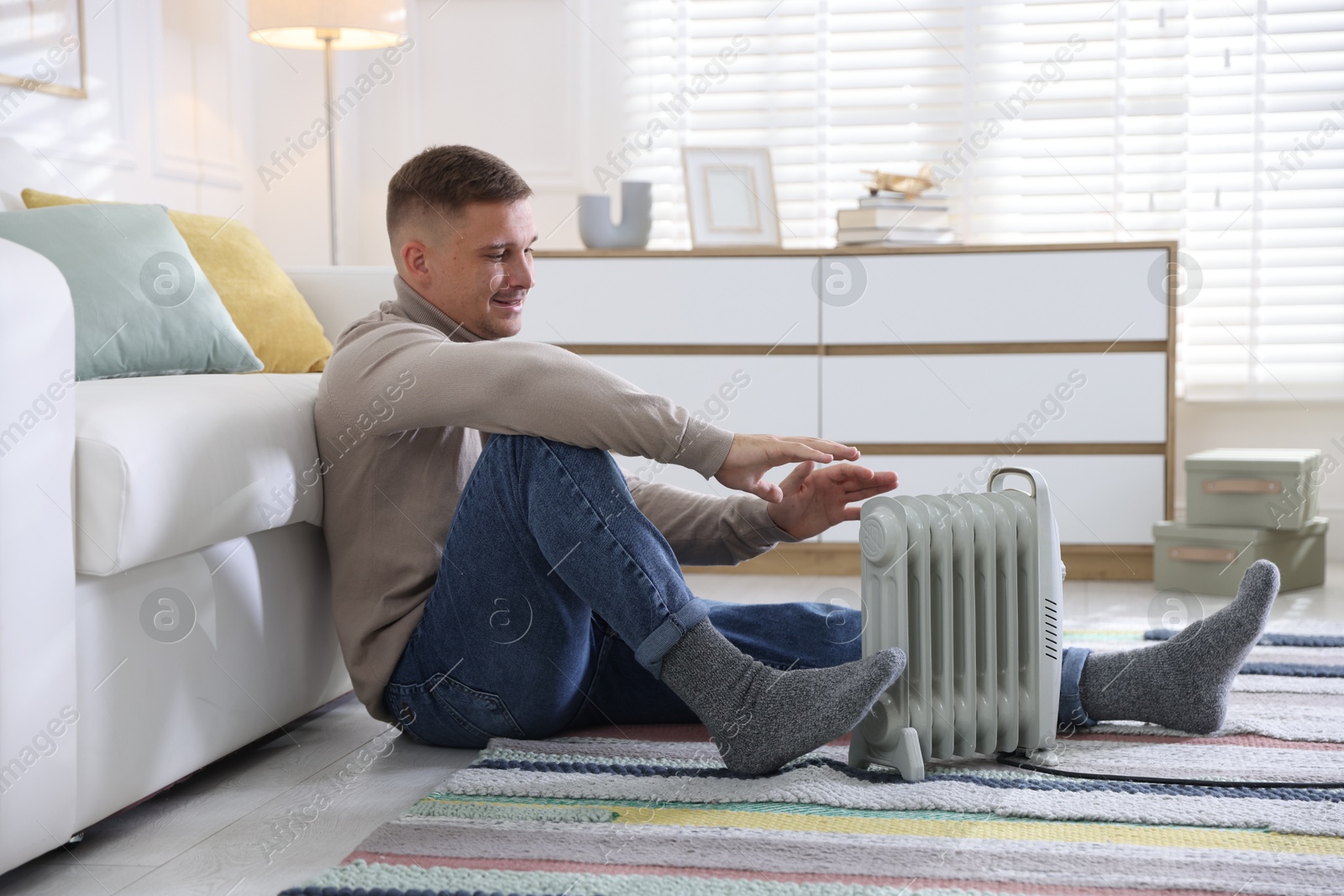 Photo of Young man near electric heater on floor at home