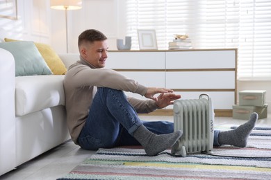 Photo of Young man near electric heater on floor at home