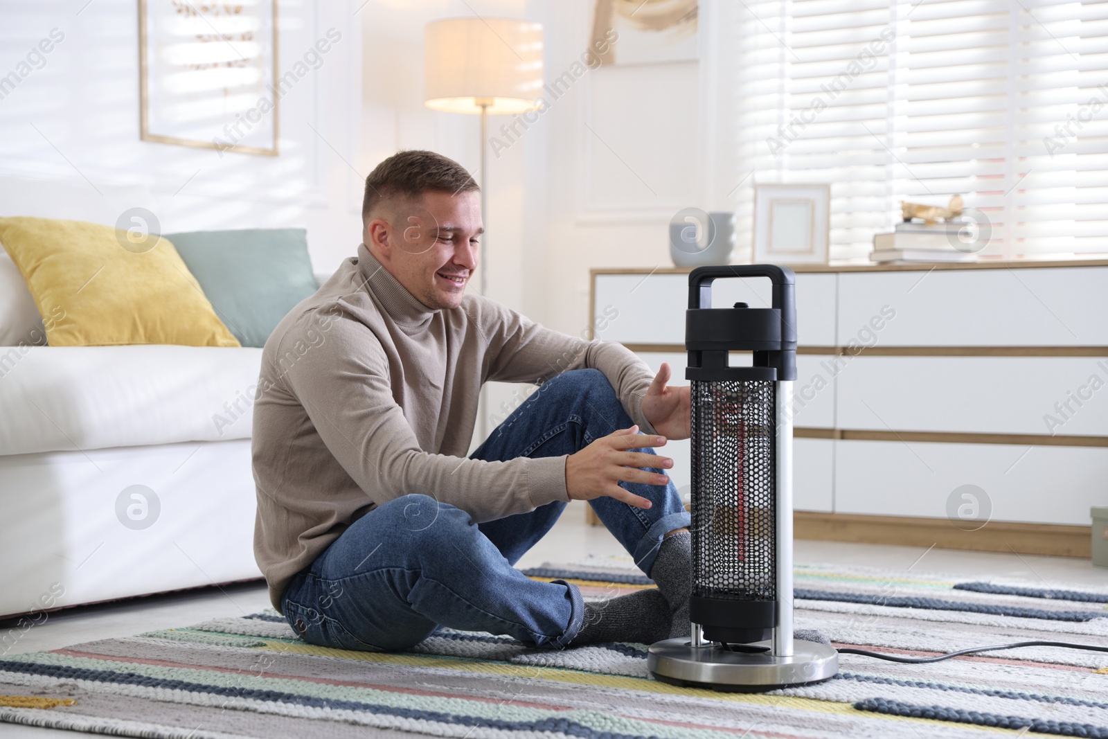 Photo of Young man near electric heater on floor at home
