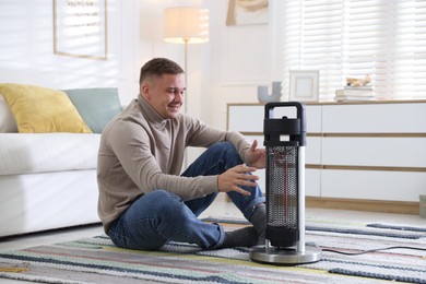 Photo of Young man near electric heater on floor at home