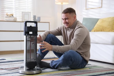 Photo of Young man near electric heater on floor at home