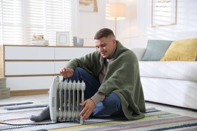Photo of Young man near electric heater on floor at home