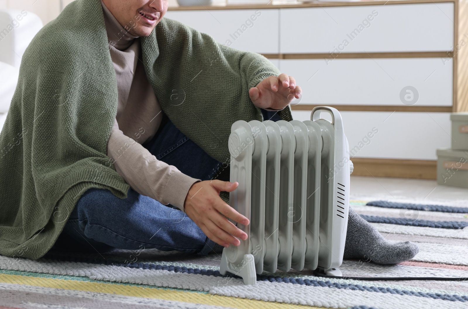 Photo of Young man near electric heater on floor at home, closeup