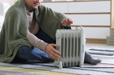 Photo of Young man near electric heater on floor at home, closeup