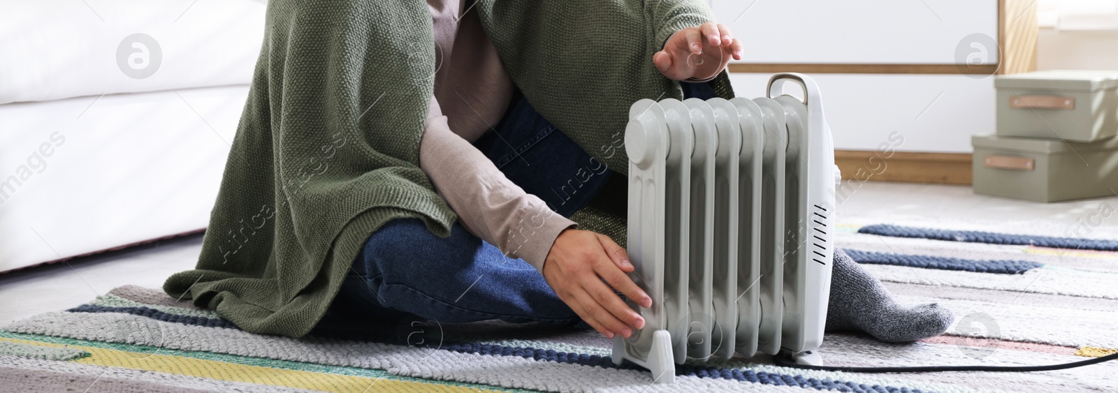 Photo of Young man near electric heater on floor at home, closeup
