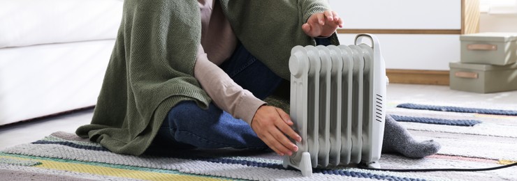 Photo of Young man near electric heater on floor at home, closeup