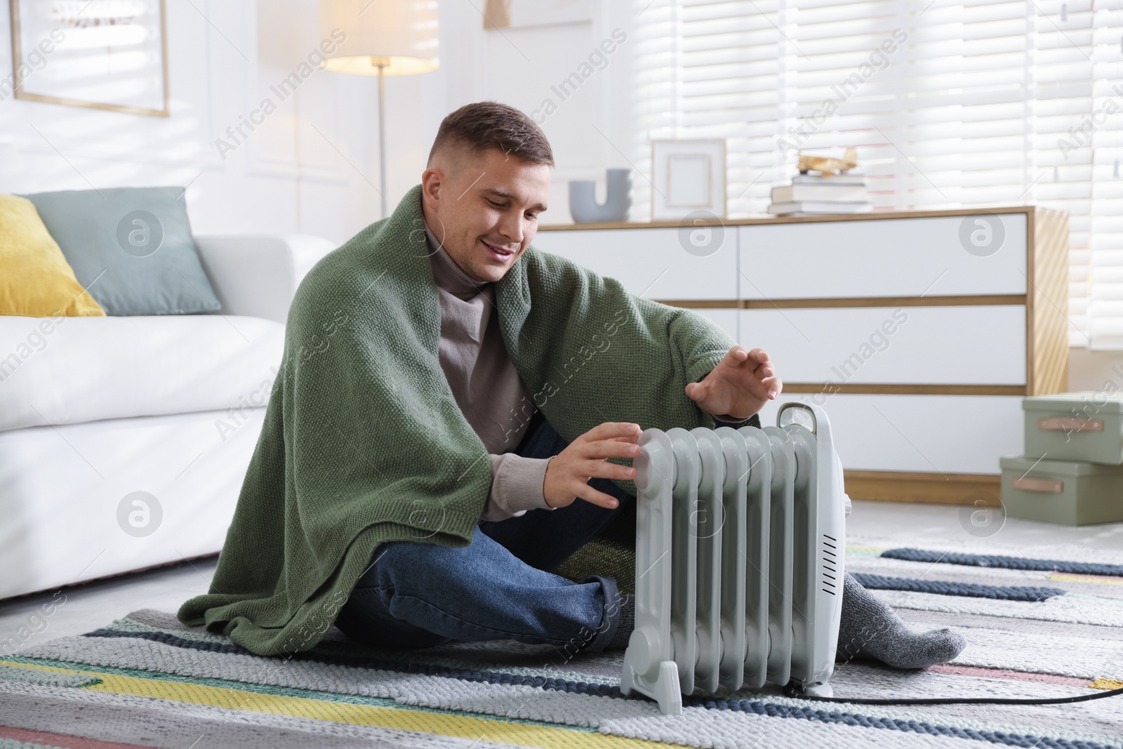 Photo of Young man near electric heater on floor at home
