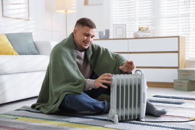 Photo of Young man near electric heater on floor at home