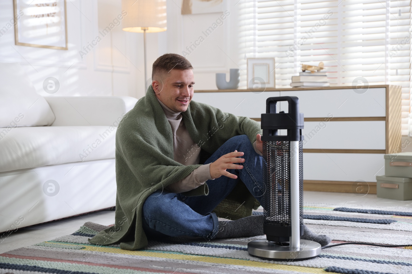 Photo of Young man near electric heater on floor at home