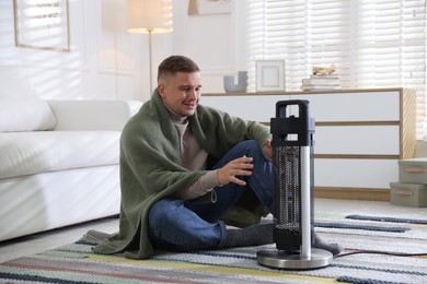 Photo of Young man near electric heater on floor at home