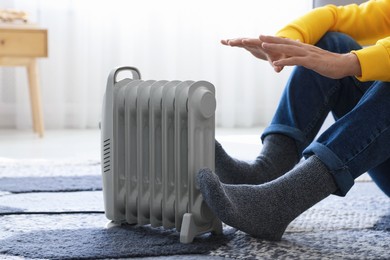 Photo of Young man near electric heater on floor at home, closeup