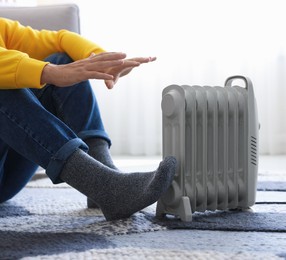 Photo of Young man near electric heater on floor at home, closeup