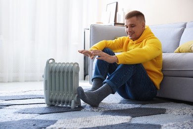 Photo of Young man near electric heater on floor at home