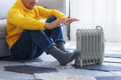 Photo of Young man near electric heater on floor at home, closeup