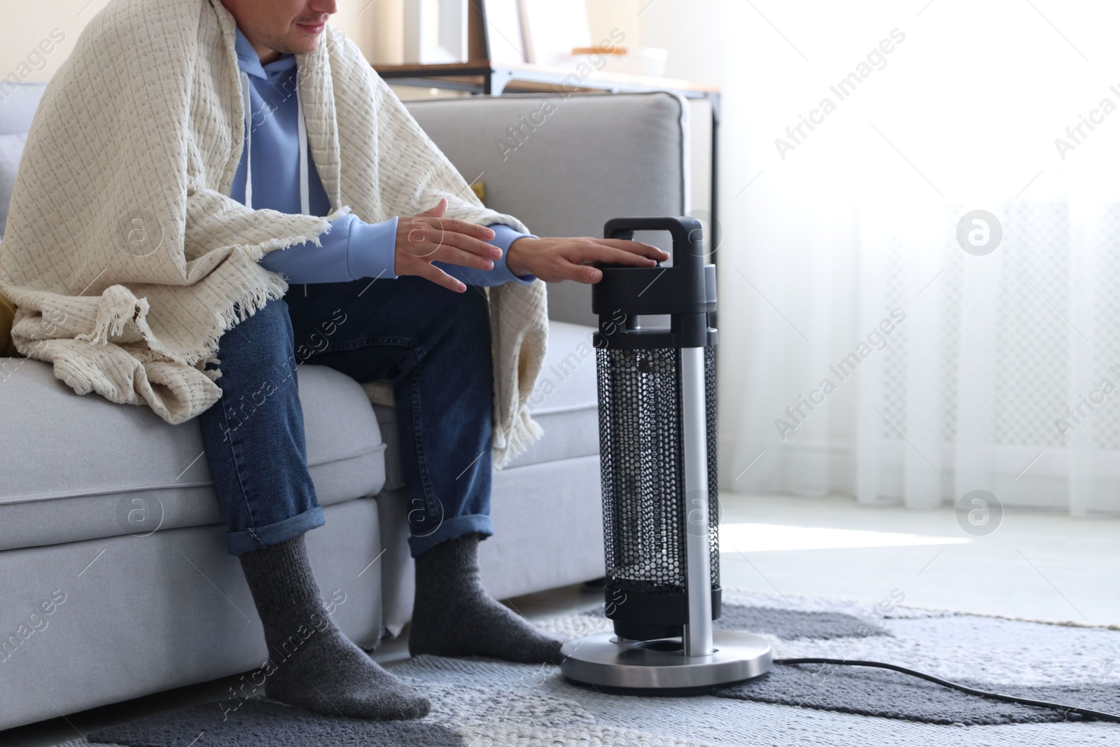 Photo of Young man with blanket near electric heater at home, closeup