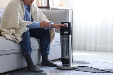Photo of Young man with blanket near electric heater at home, closeup