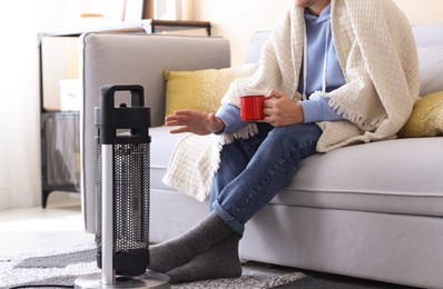 Photo of Young man with cup of drink near electric heater at home, closeup