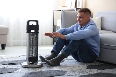 Photo of Young man near electric heater on floor at home