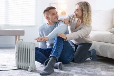 Photo of Happy couple near electric heater on floor at home