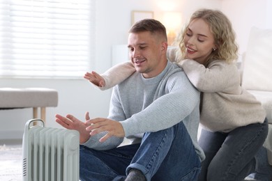 Photo of Happy couple near electric heater on floor at home