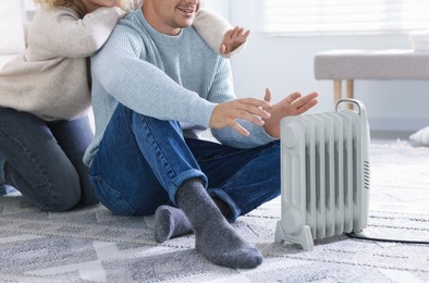 Photo of Happy couple near electric heater on floor at home, closeup
