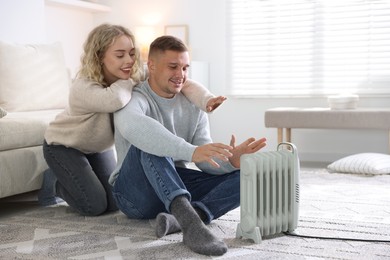 Photo of Happy couple near electric heater on floor at home