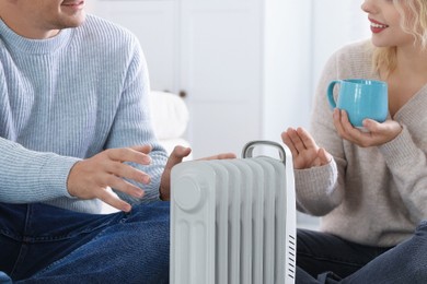 Photo of Happy couple near electric heater on floor at home, closeup