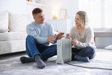 Photo of Happy couple near electric heater on floor at home