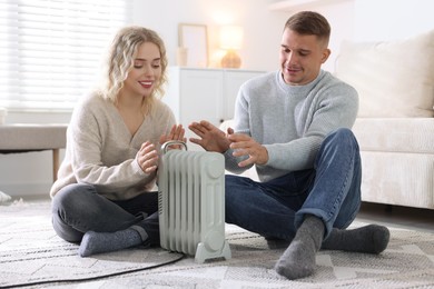 Photo of Happy couple near electric heater on floor at home