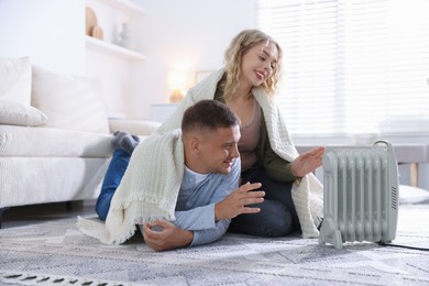 Photo of Happy couple near electric heater on floor at home