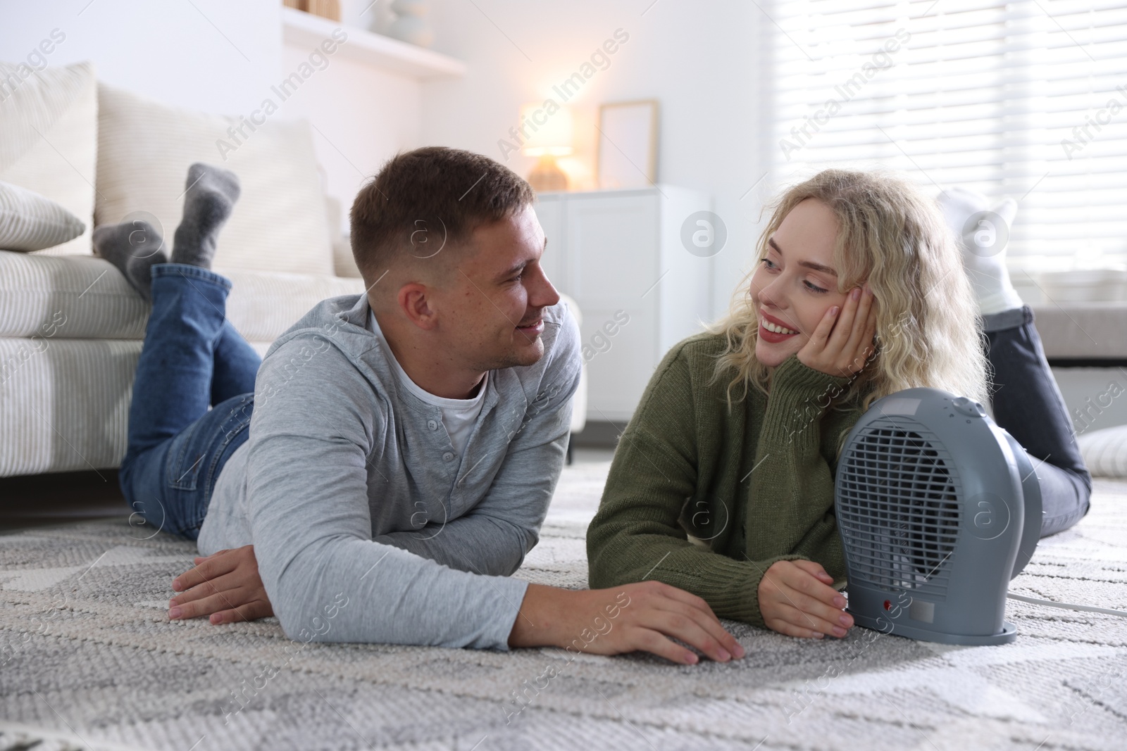 Photo of Happy couple near electric heater on floor at home