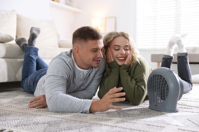 Photo of Happy couple near electric heater on floor at home