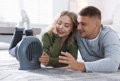 Photo of Happy couple near electric heater on floor at home