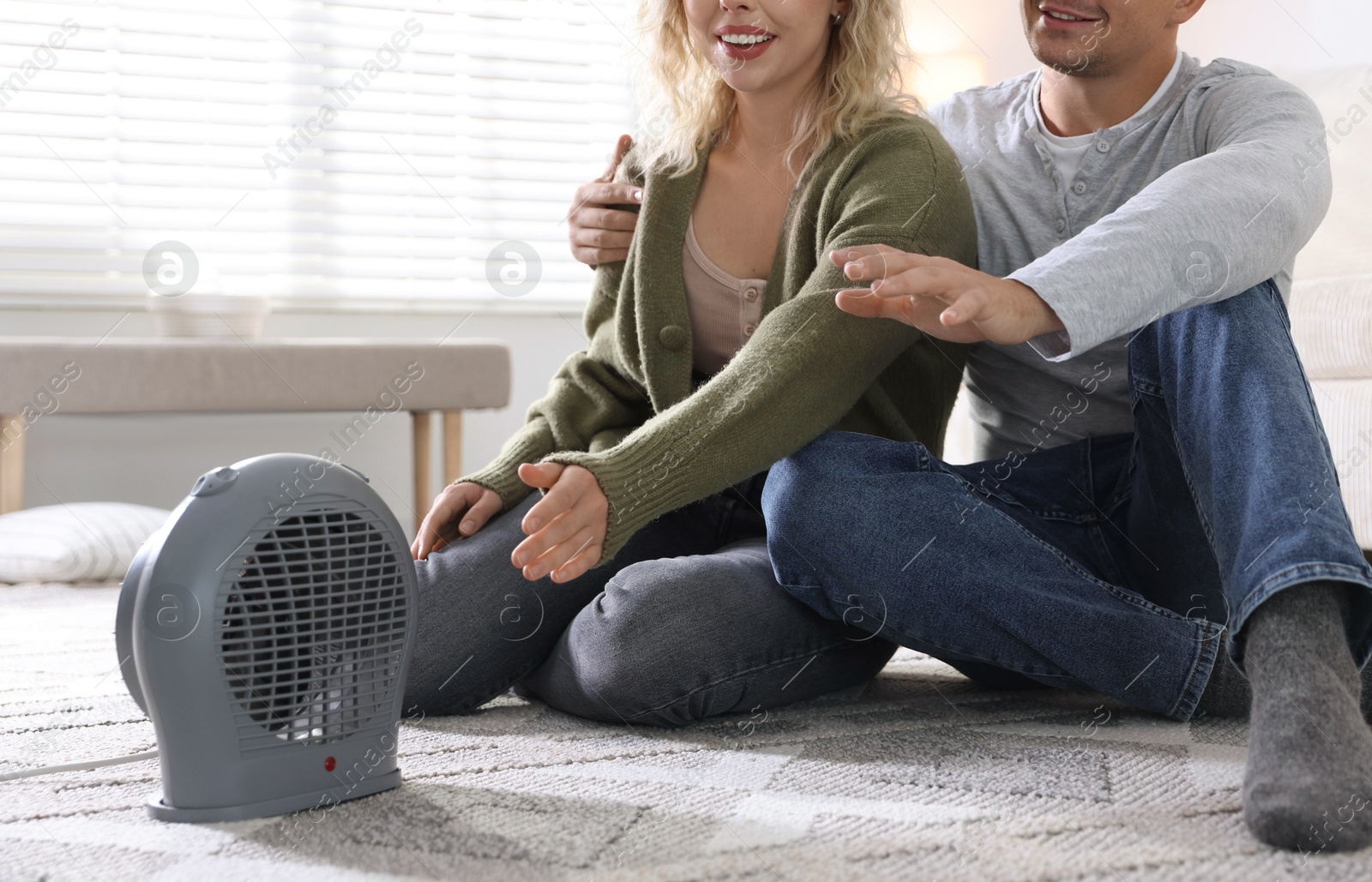 Photo of Happy couple near electric heater on floor at home, closeup