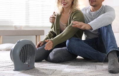 Photo of Happy couple near electric heater on floor at home, closeup
