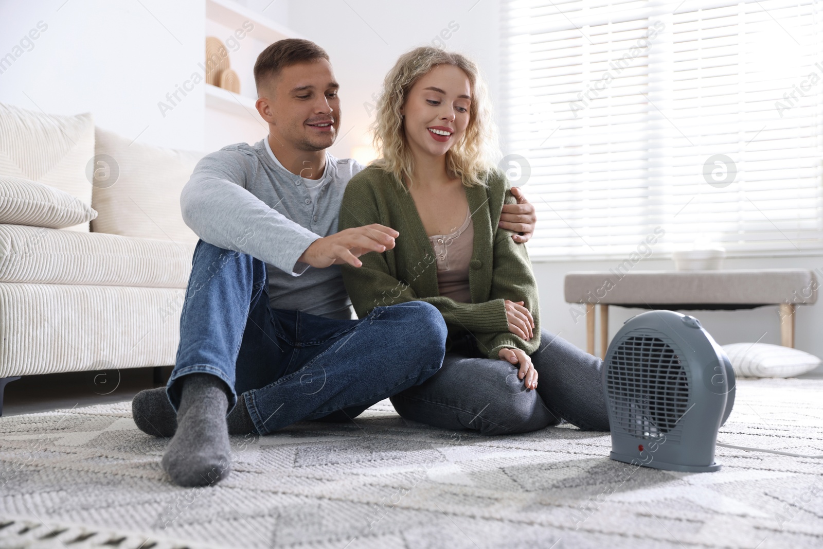 Photo of Happy couple near electric heater on floor at home