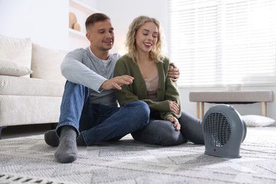 Photo of Happy couple near electric heater on floor at home