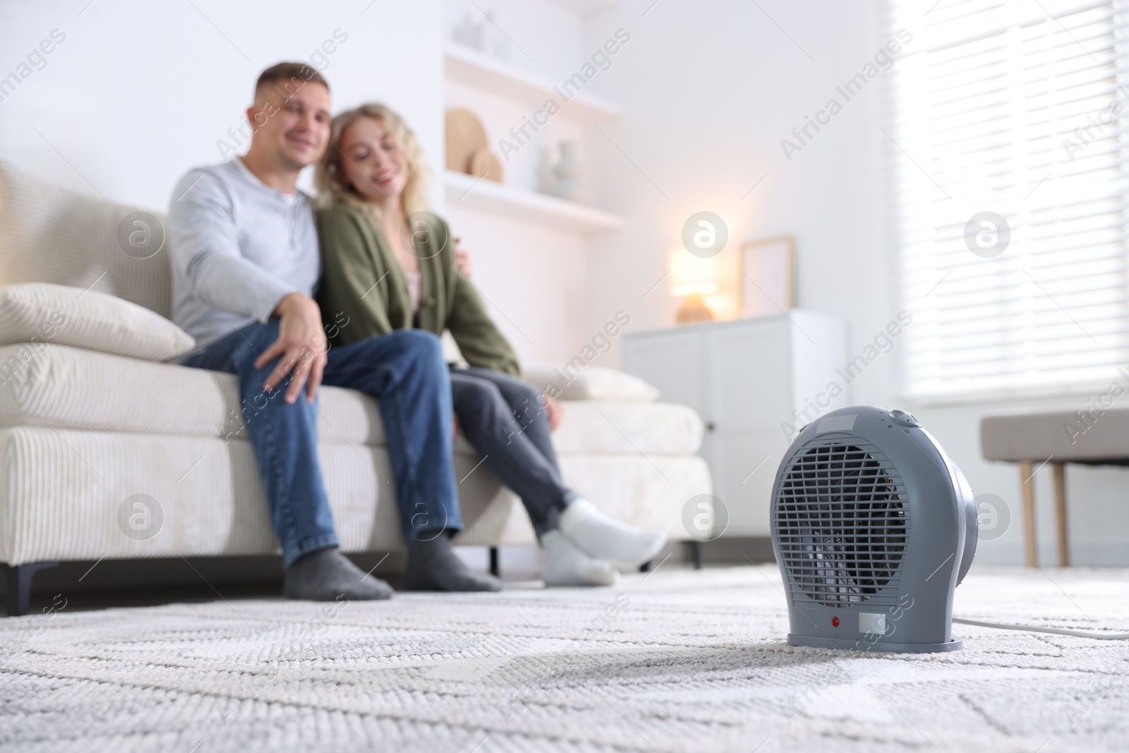 Photo of Happy couple on sofa near electric heater at home, selective focus