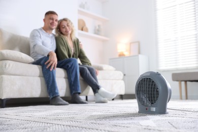 Photo of Happy couple on sofa near electric heater at home, selective focus