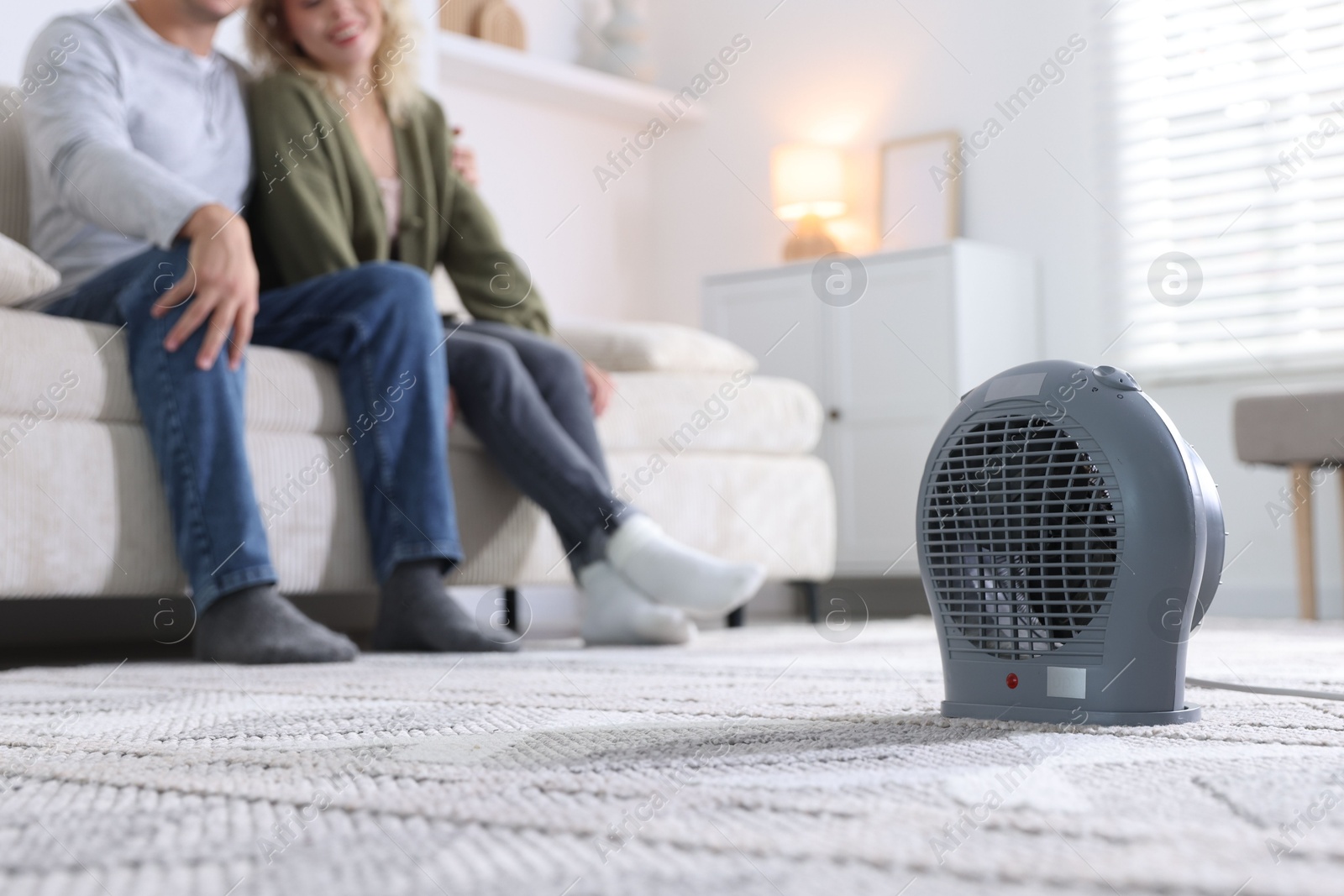 Photo of Happy couple on sofa near electric heater at home, selective focus