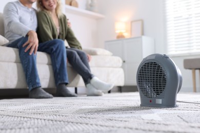 Photo of Happy couple on sofa near electric heater at home, selective focus