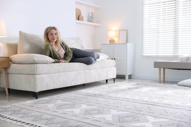 Photo of Happy young woman resting on sofa at home, space for text