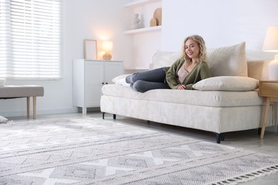 Photo of Happy young woman resting on sofa at home, space for text