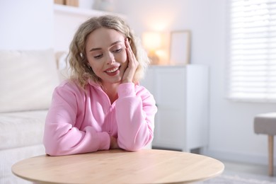 Photo of Happy young woman sitting at wooden table and looking at something indoors, space for text