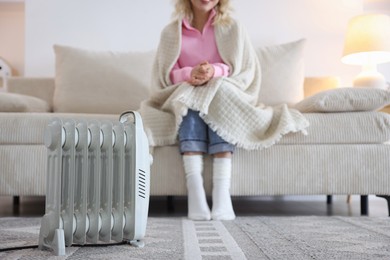 Photo of Young woman on sofa near electric heater at home, selective focus