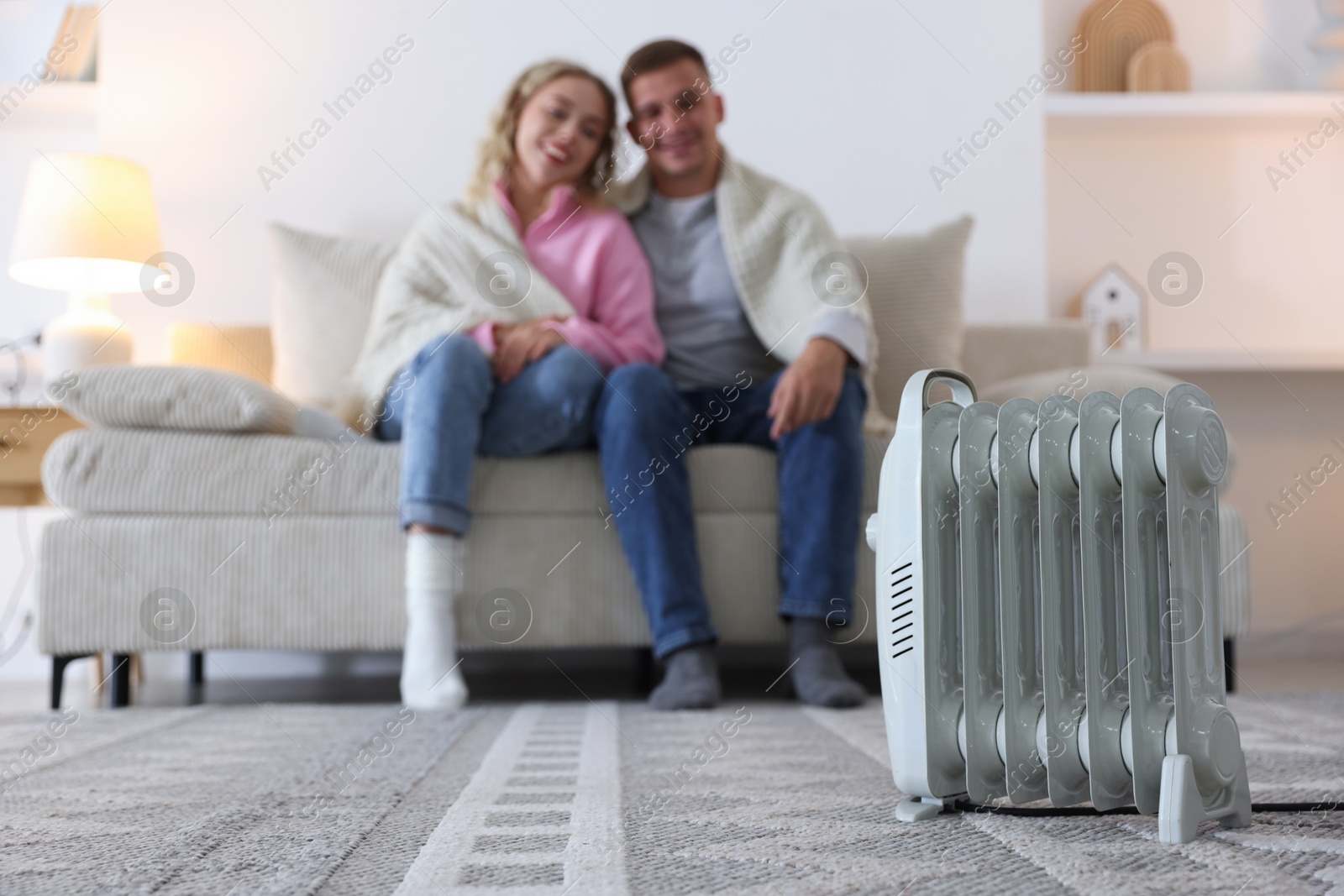Photo of Happy couple on sofa near electric heater at home, selective focus