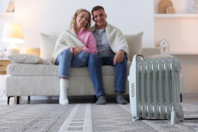 Photo of Happy couple on sofa near electric heater at home, selective focus