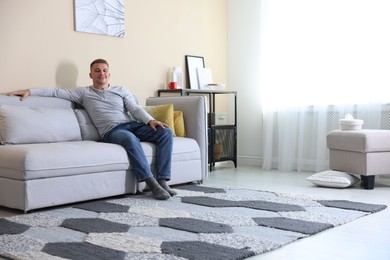 Photo of Happy young man resting on sofa at home, space for text